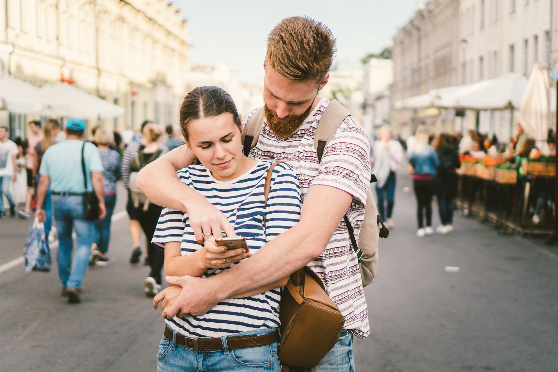 Mann umarmt Frau von hinten und zeigt auf ihr Handy